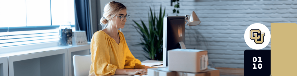 A person at a desk with office supplies, wearing a yellow top, working on a computer