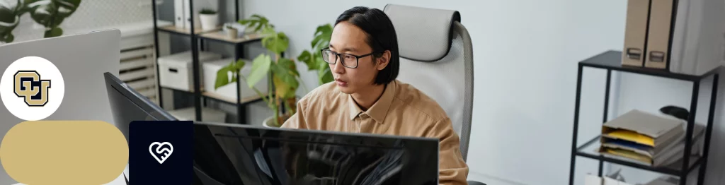 Person working at a desk with multiple monitors and office supplies, indoor office setting.

